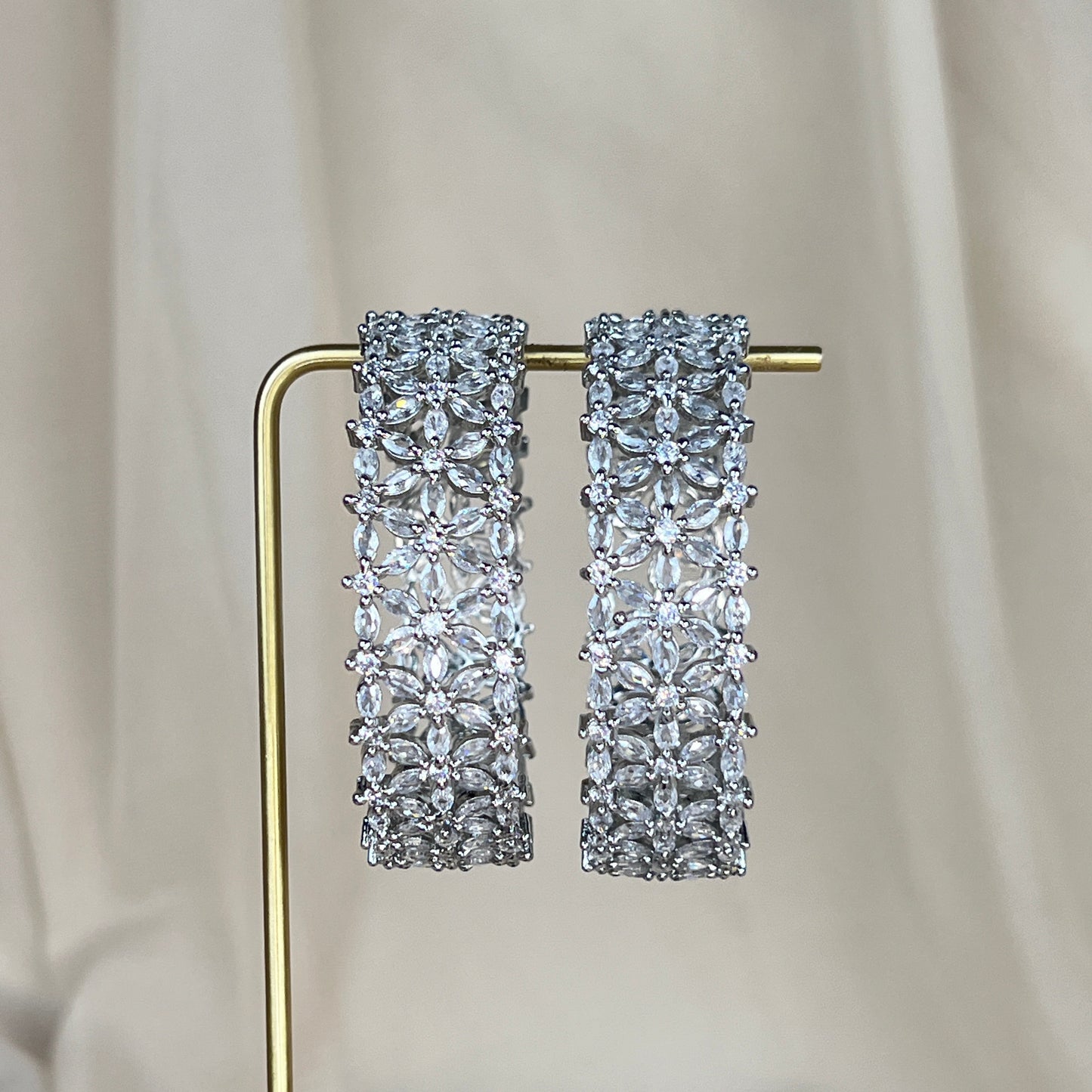 Pair of silver american diamond bangles on a gold stand against a neutral background