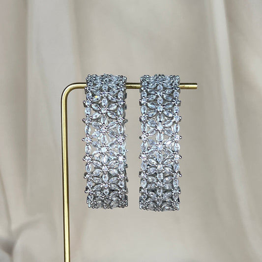 Pair of silver american diamond bangles on a gold stand against a neutral background
